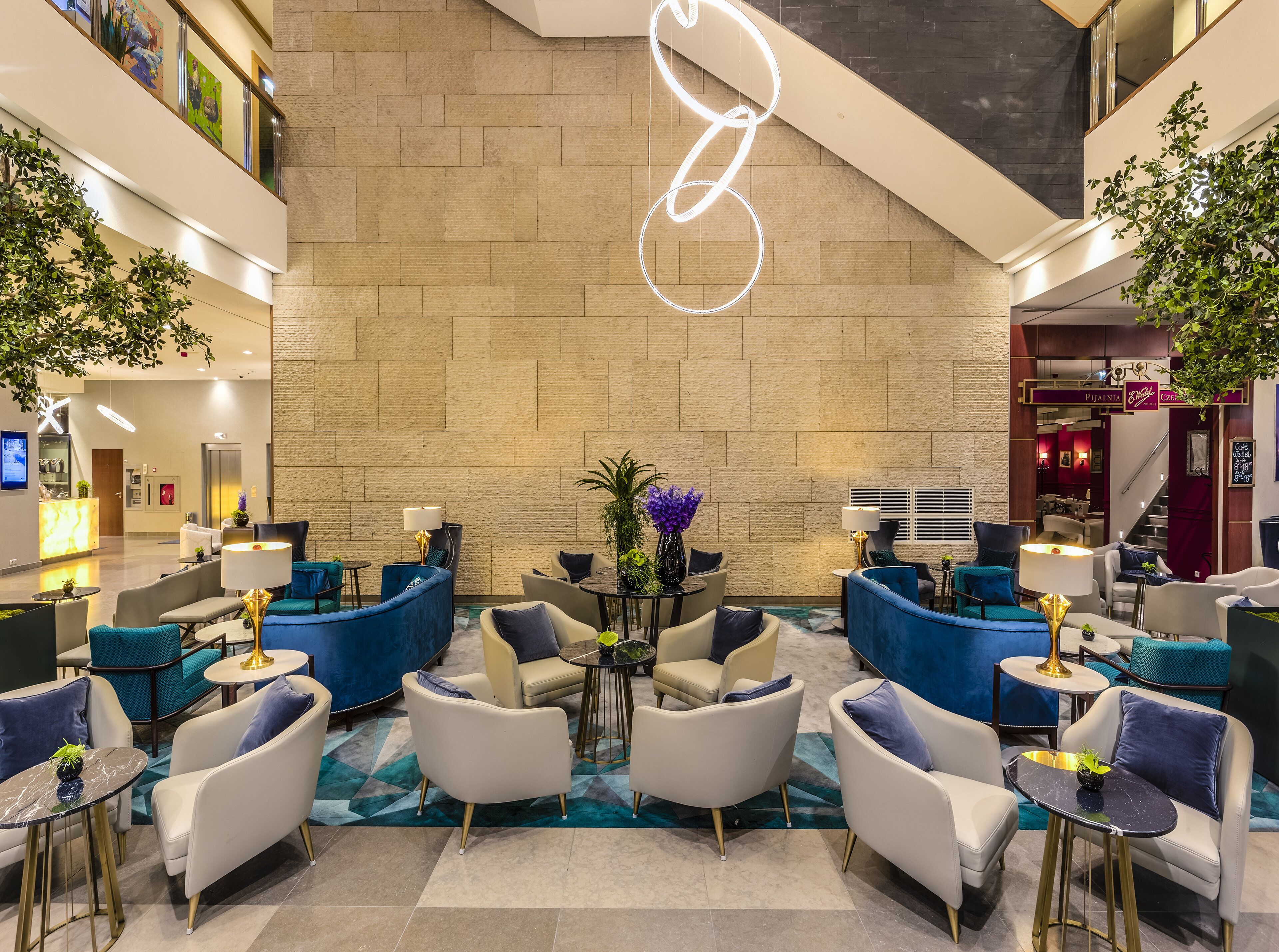 Eine moderne Lobby mit hoher Decke, einer großen Wand mit einer besonderen Leuchte und einer Mischung aus Sitzbereichen mit blau und weißer Möbel.