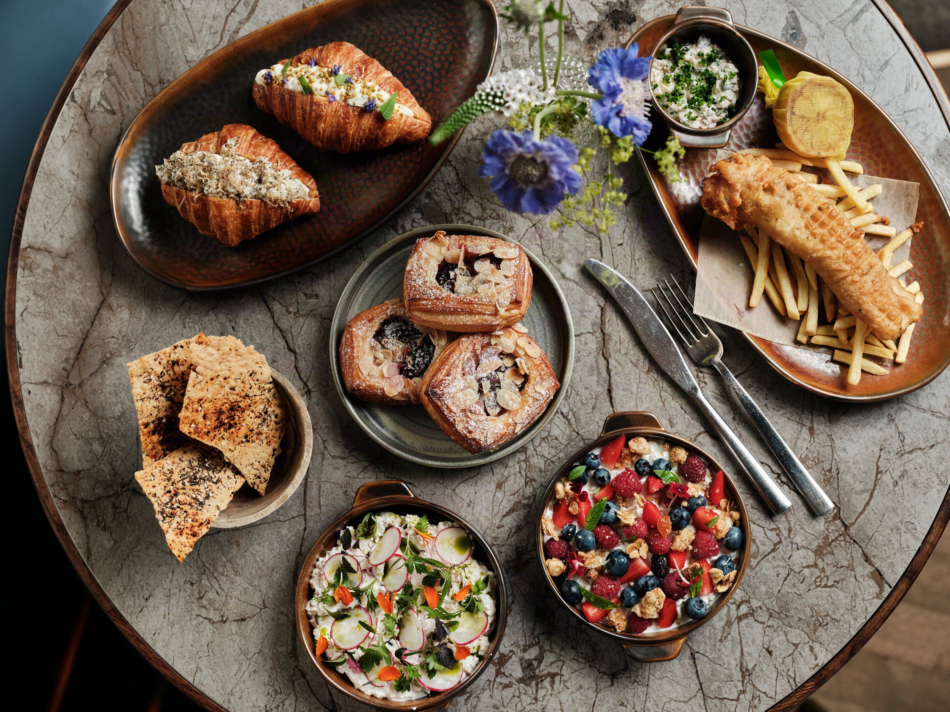 A variety of dishes including pastries, fish and chips, and a bowl of fruit salad.