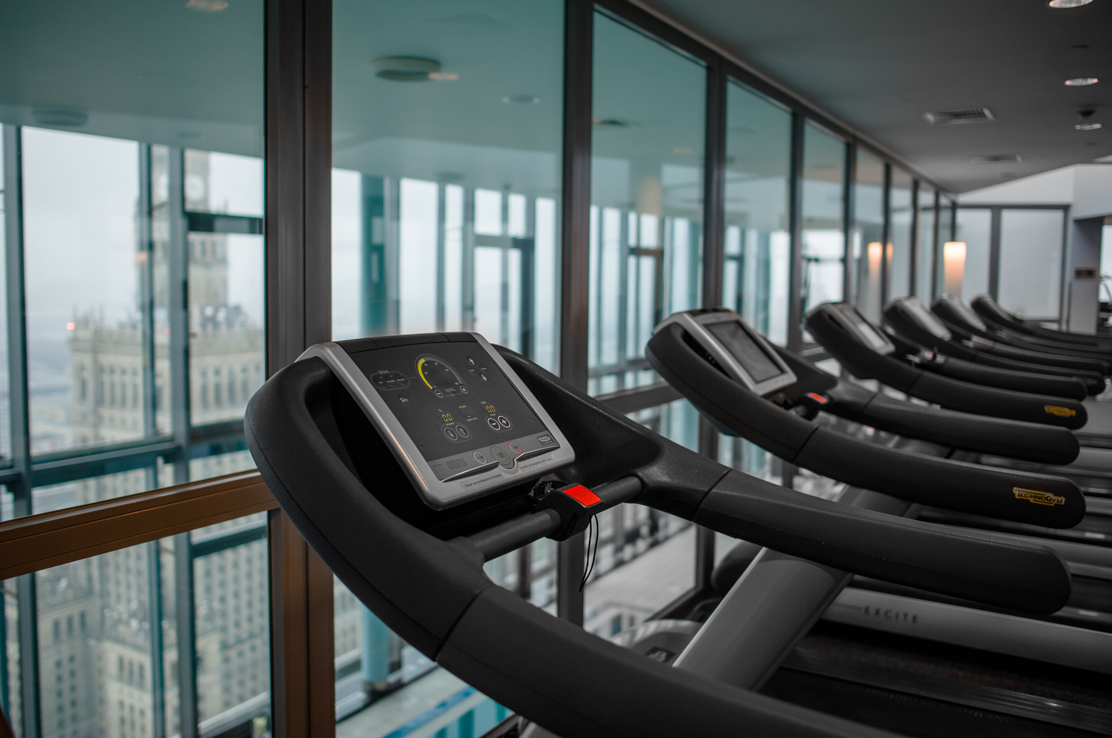 Varias bicicletas estáticas en un gimnasio con amplios ventanales y vista a la ciudad.