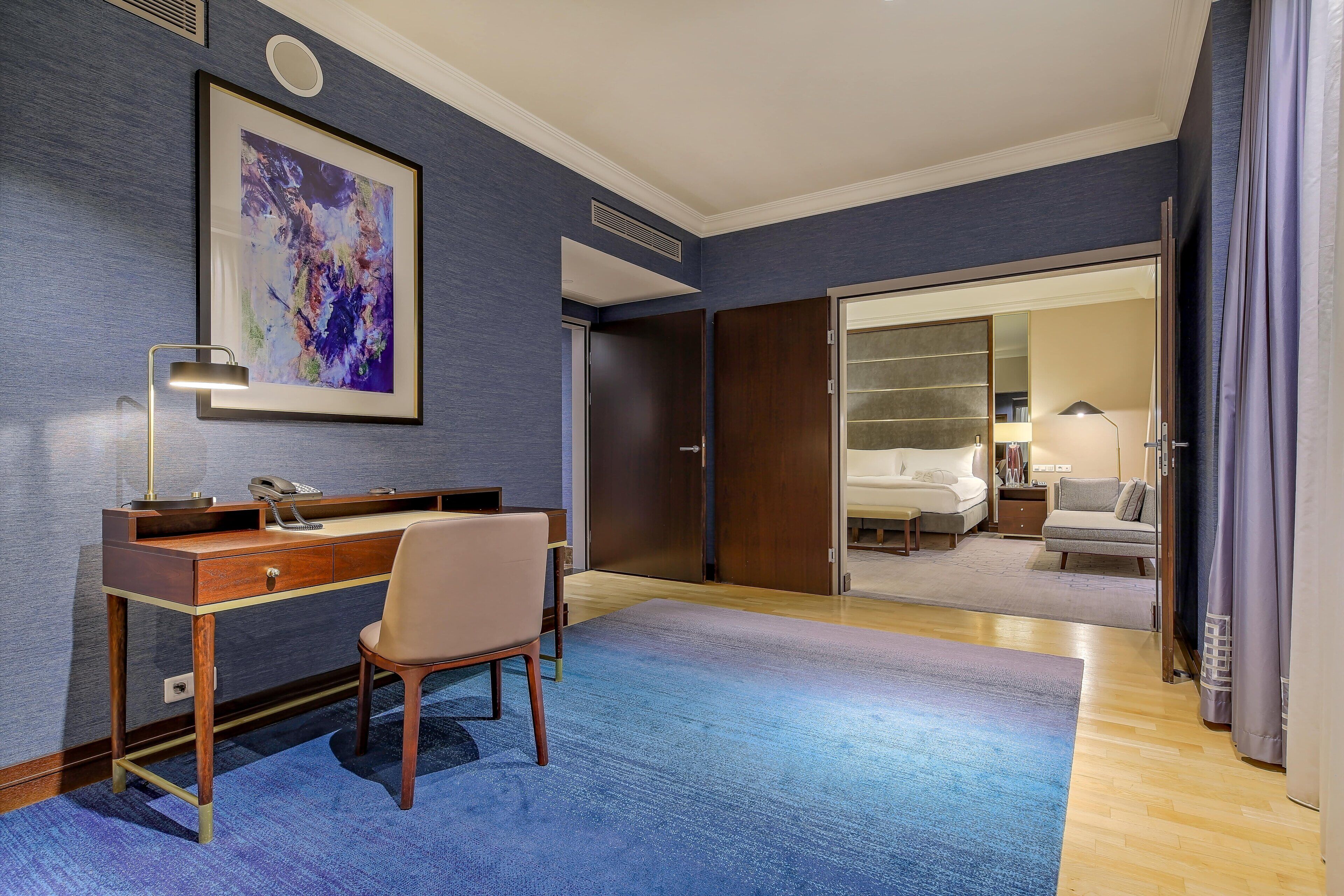 A hotel room with a desk, chair, and a bed.