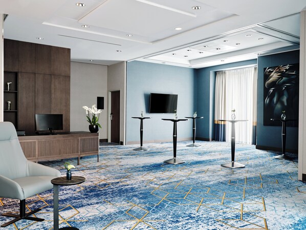 A modern hotel lobby with a seating area, a reception desk, a flat-screen TV, and a large poster on the wall.