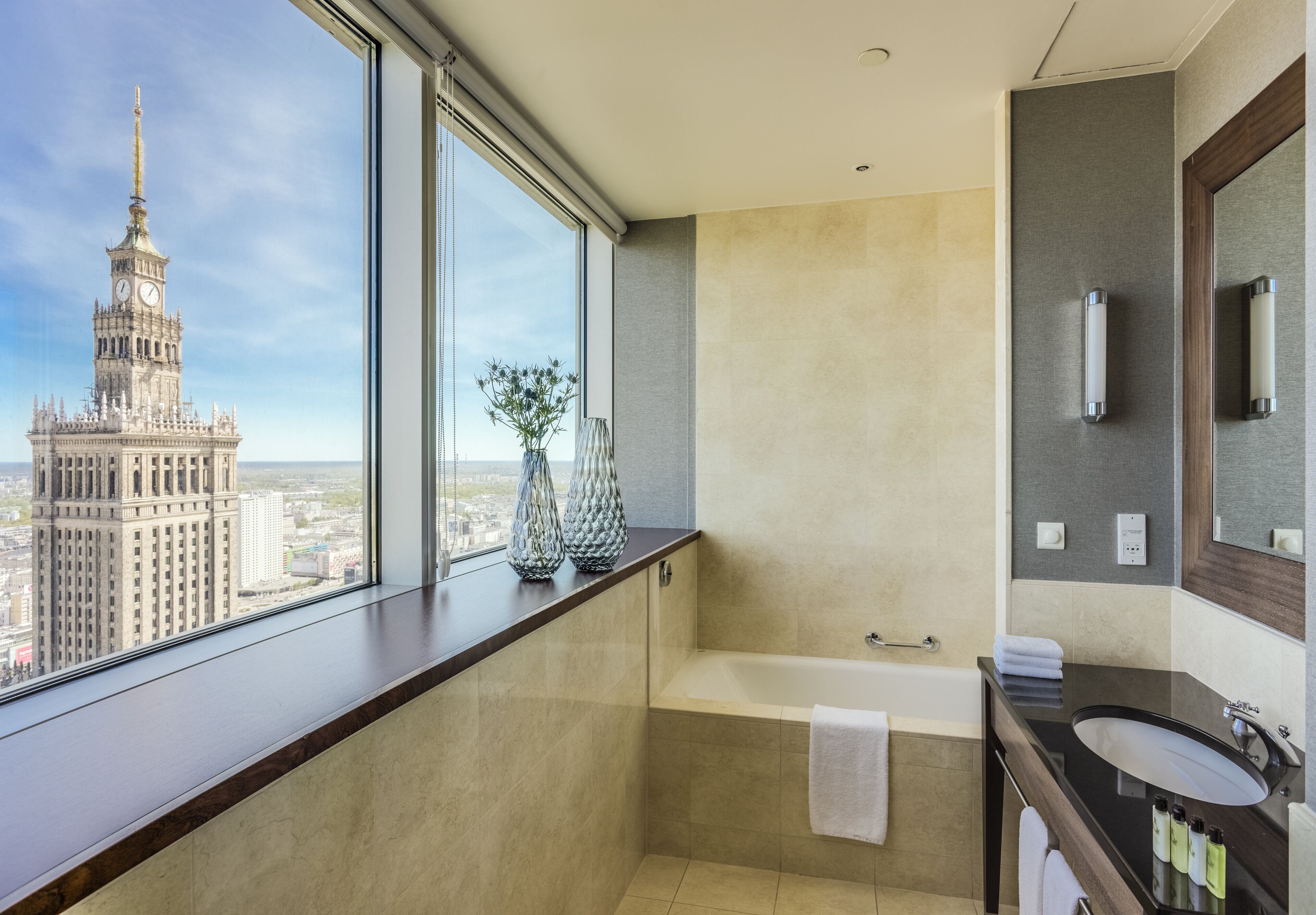 Un baño moderno con una bañera, un espejo grande y una ventana con vistas a la ciudad.