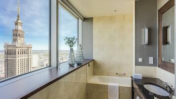 A modern bathroom with a bathtub, a large mirror, and a window overlooking a cityscape.