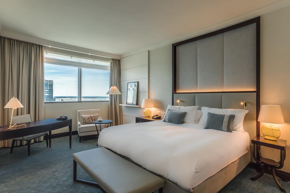 Camera d'albergo con un letto grande, una scrivania, una sedia, una panca e vista sulla città dalla finestra.