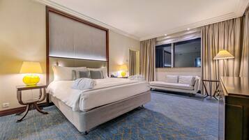 A hotel room with a large bed, bedside tables with lamps, a sofa, a desk, and a large window with curtains.