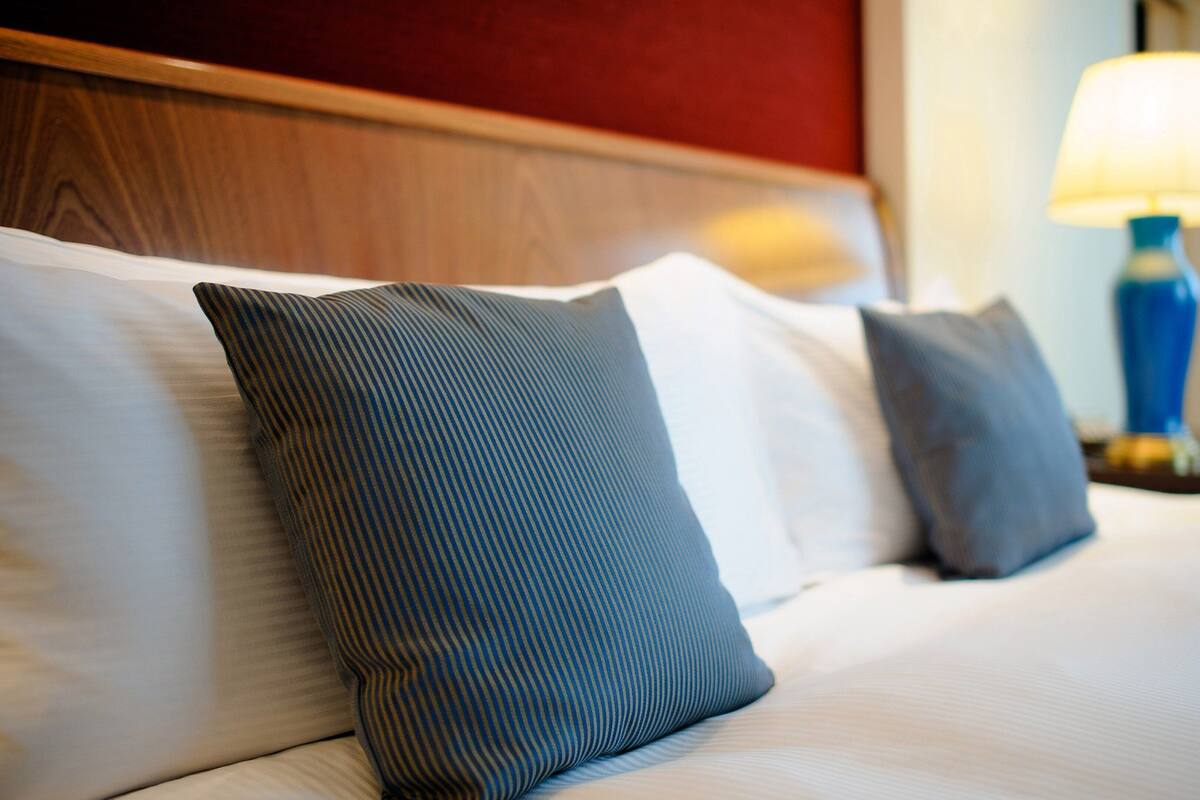Una cama bien hecha con almohadas a rayas y una lámpara sobre una mesita de noche.