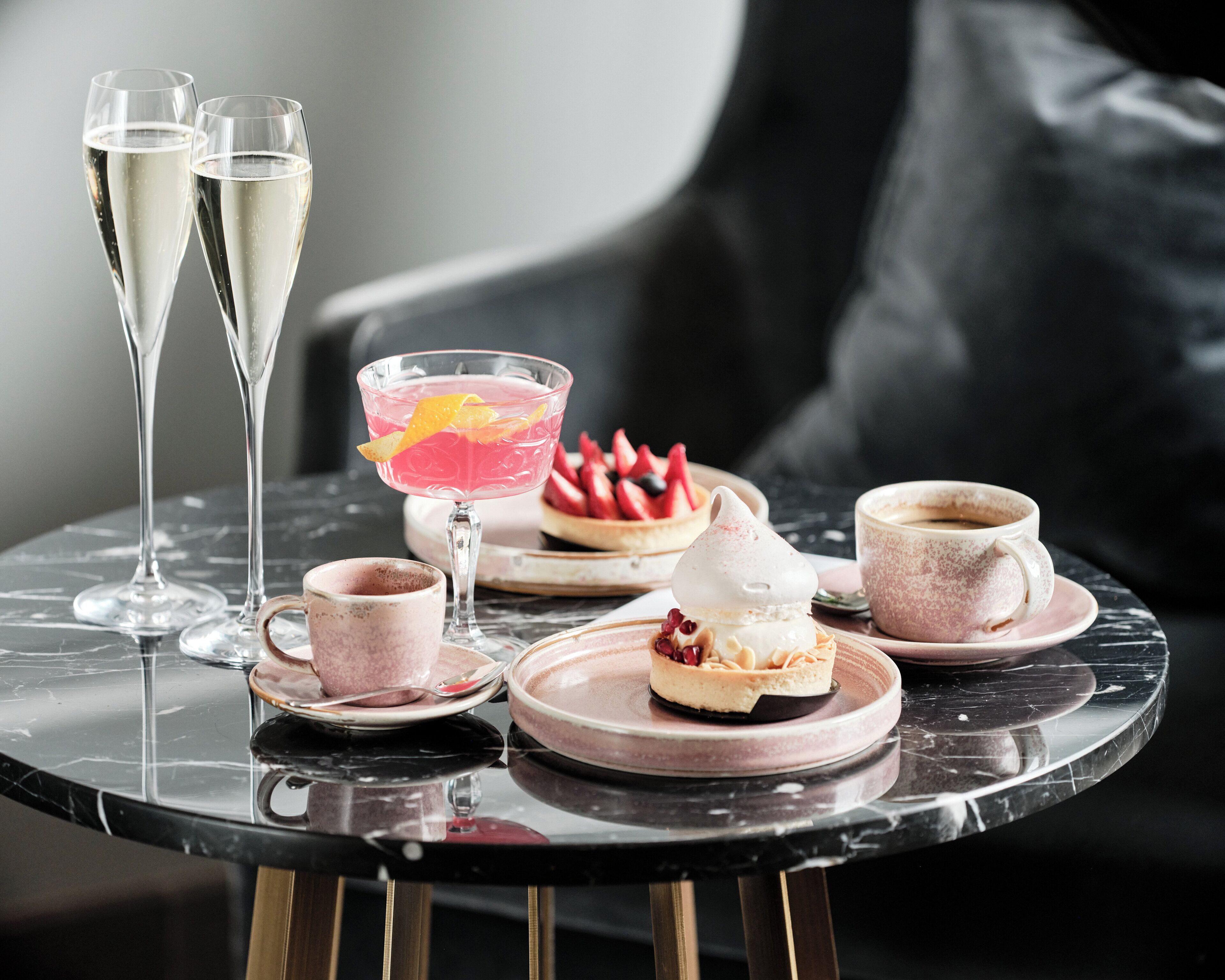 A table with two champagne flutes, a cocktail glass, a cup of coffee, and a dessert plate with a pastry and fruit.