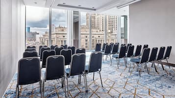 A conference room with rows of chairs, large windows with a city view, and a patterned carpet.