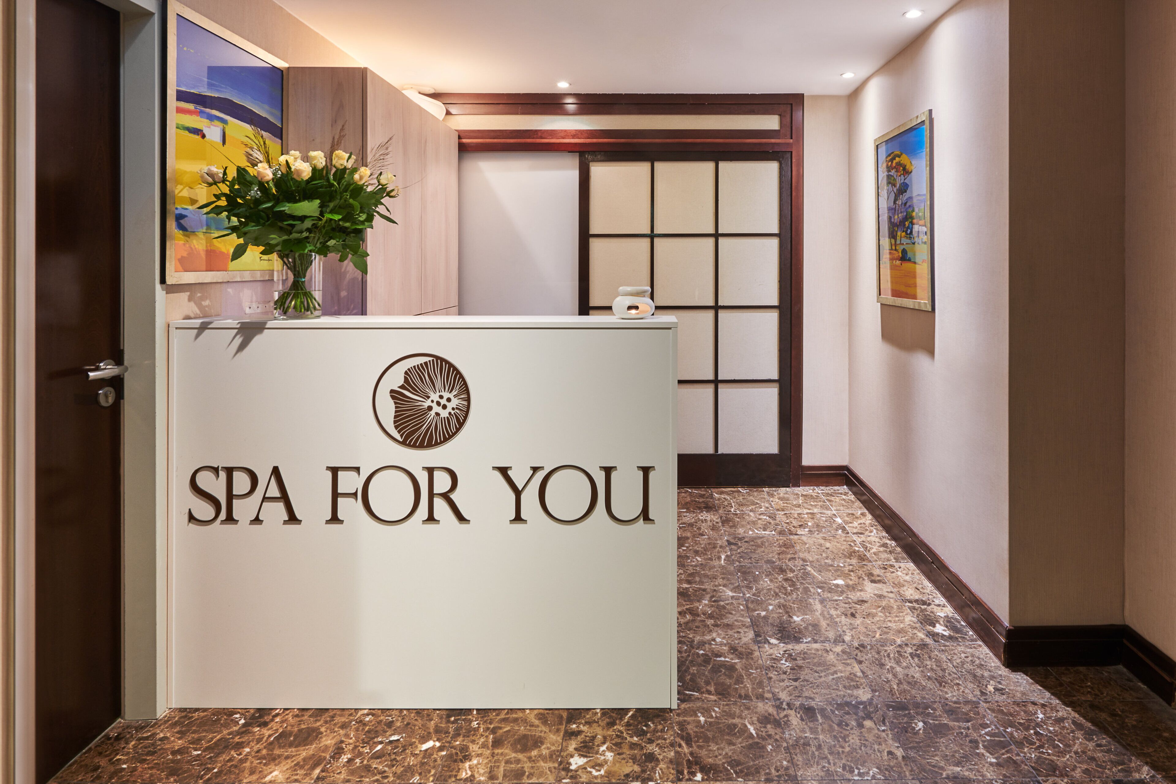 A reception desk with "SPA FOR YOU" signage, a vase of flowers, and a painting on the wall.