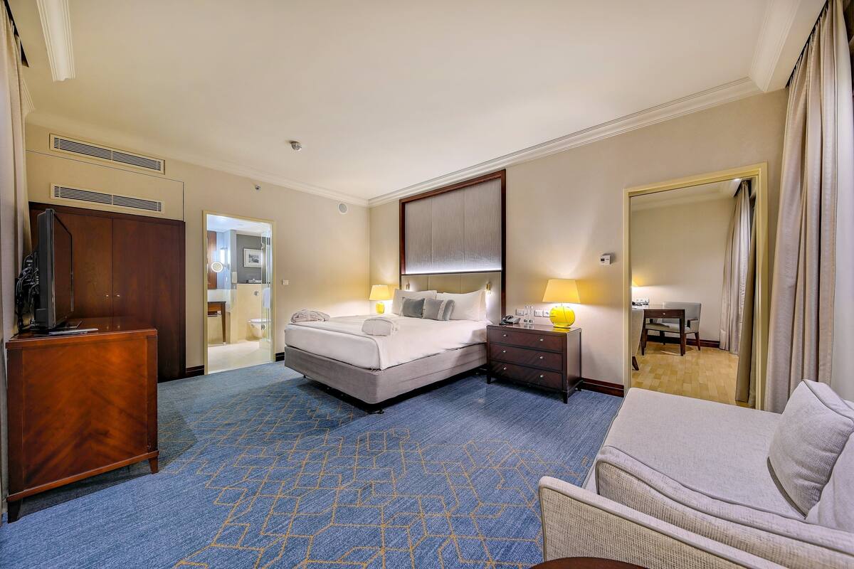 Una habitación de hotel con una cama grande, un escritorio, una silla, un aparador y un espejo.