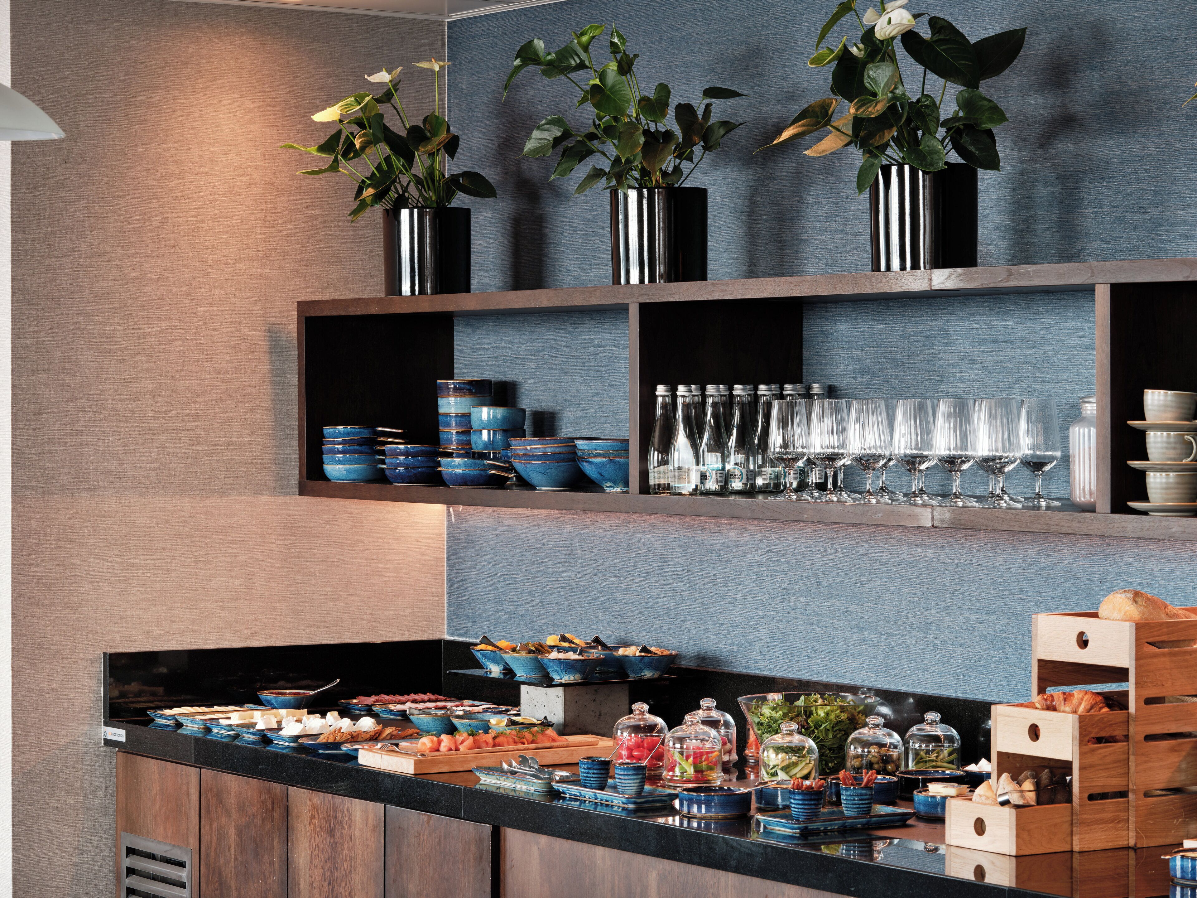 A buffet setup with various food items, glassware, and decorative plants.