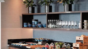 A buffet setup with various food items, glassware, and decorative plants.