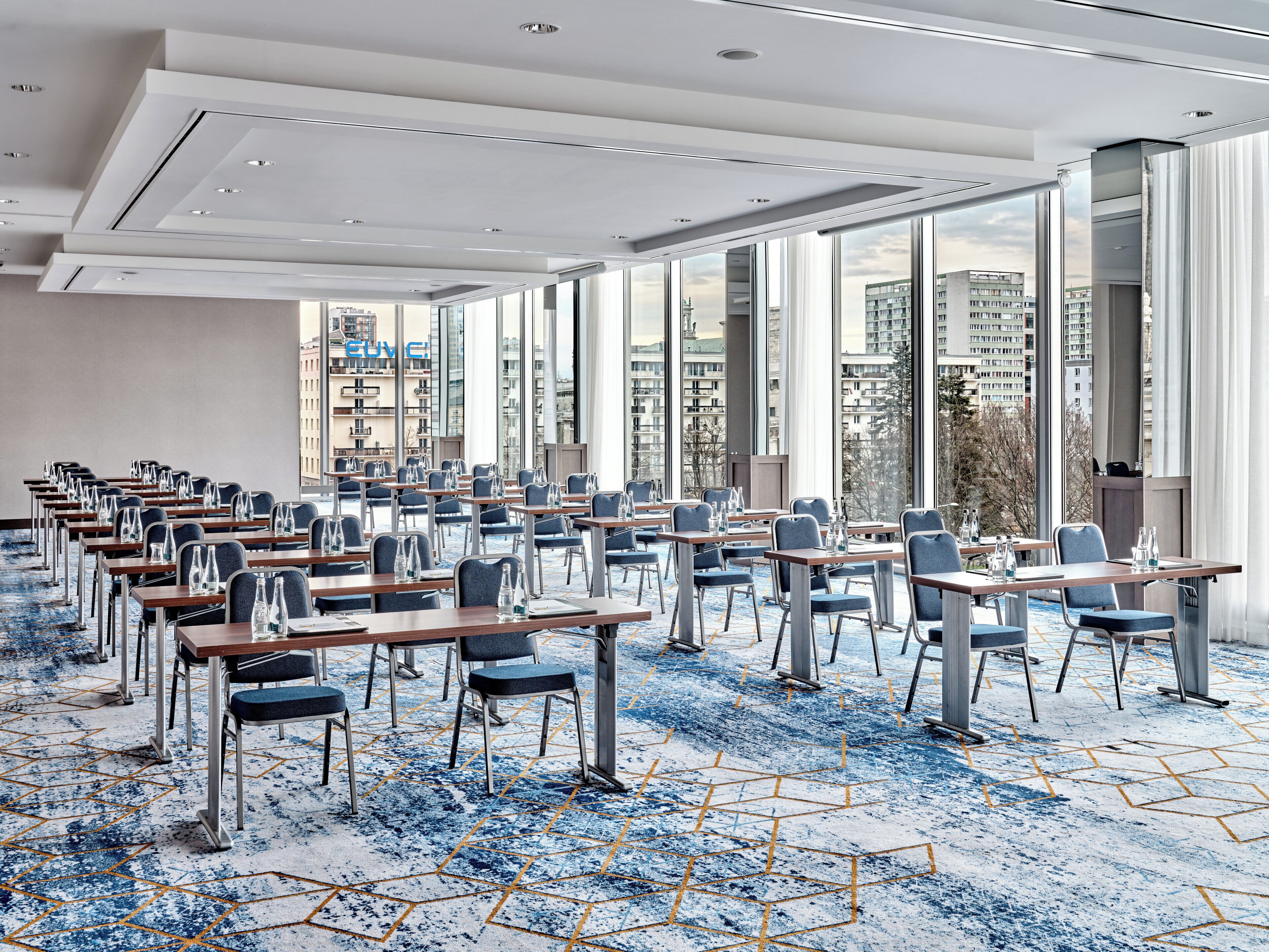 A conference room with tables and chairs, large windows, and a city view.