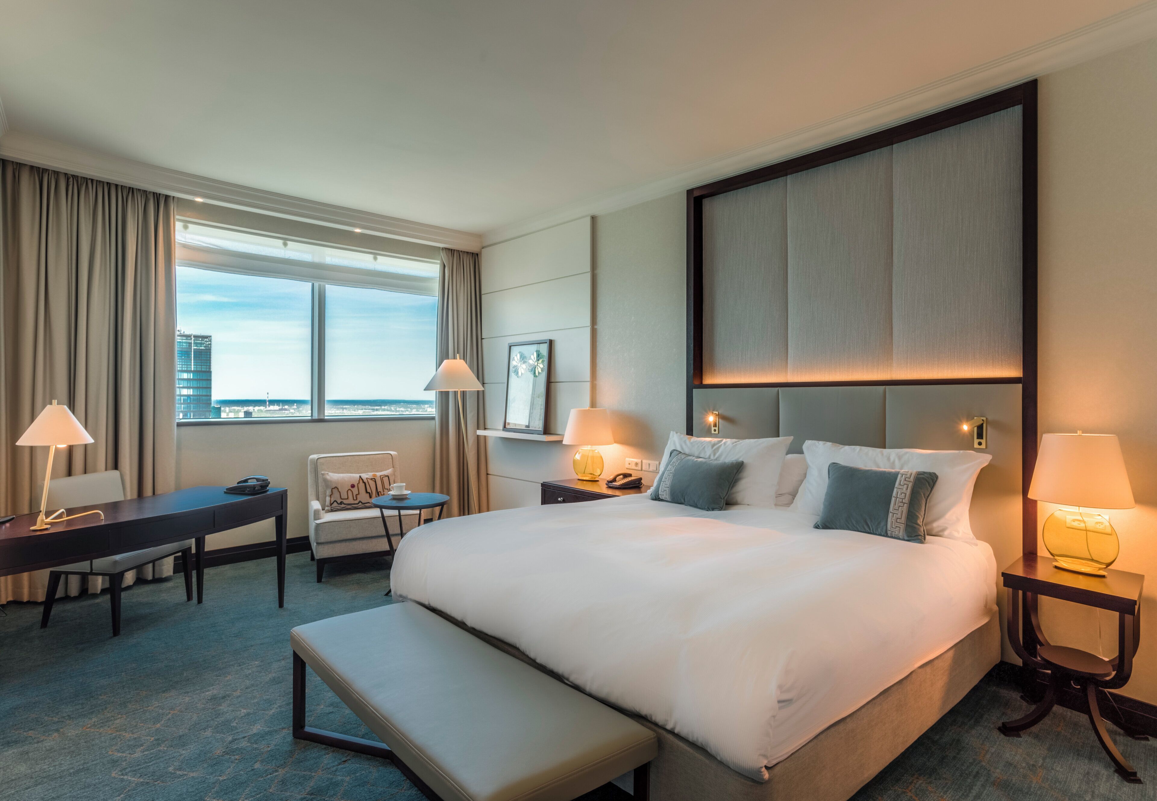 A hotel room with a large bed, a desk, a chair, and a view of the city.