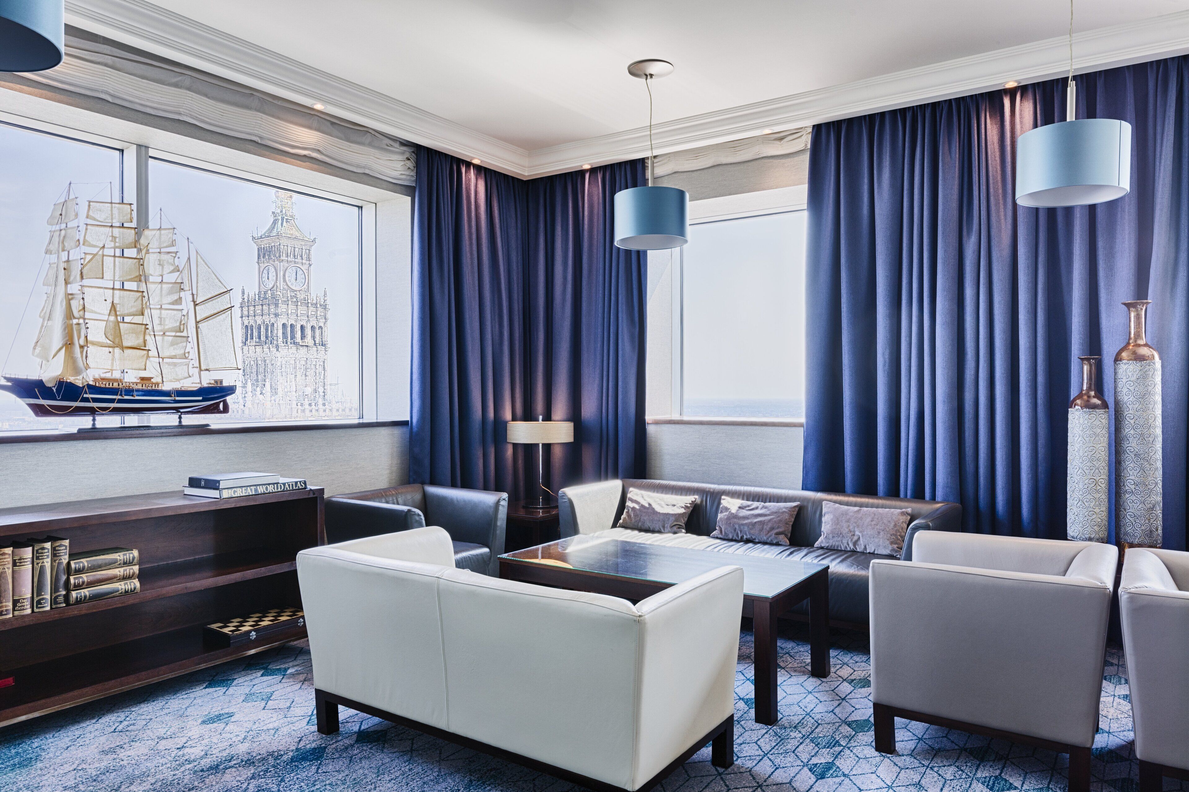 Habitación de hotel moderna con un ventanal grande, una estantería, un sofá blanco, una mesa de centro y una lámpara.