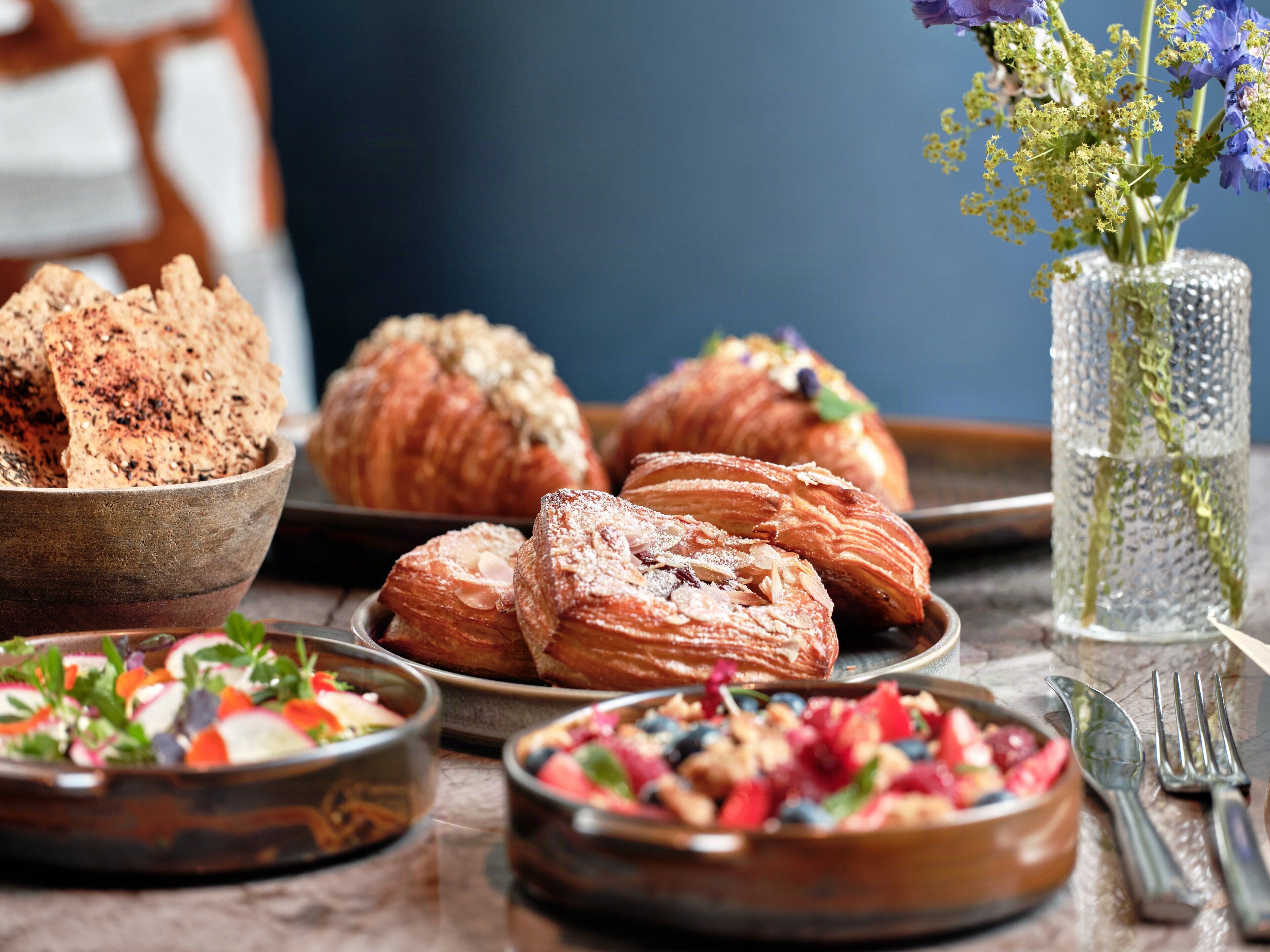A table with pastries, a bowl of salad, and a vase with flowers.