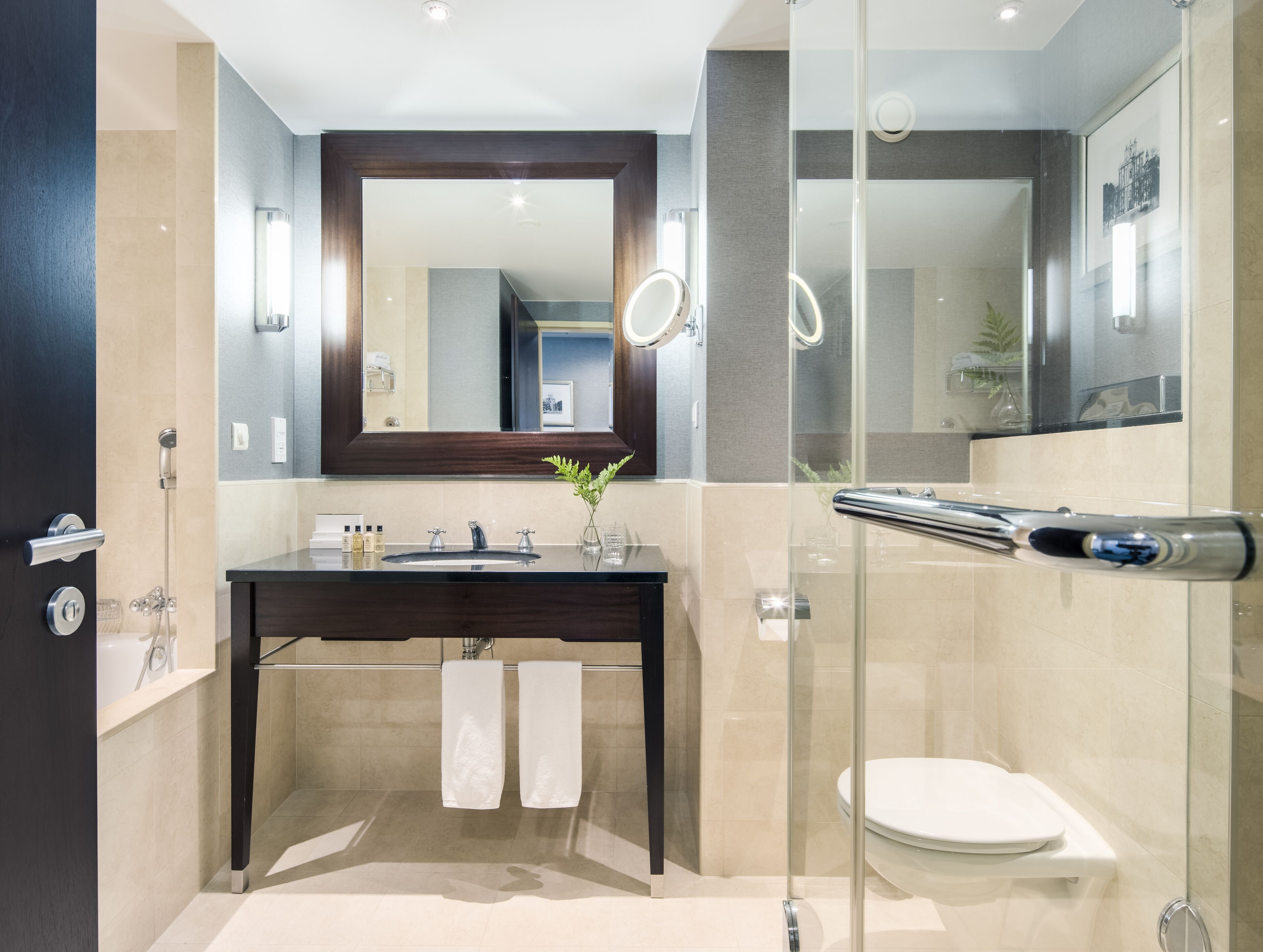 A modern bathroom with a dark vanity, a large mirror, a glass shower enclosure, and a white toilet.