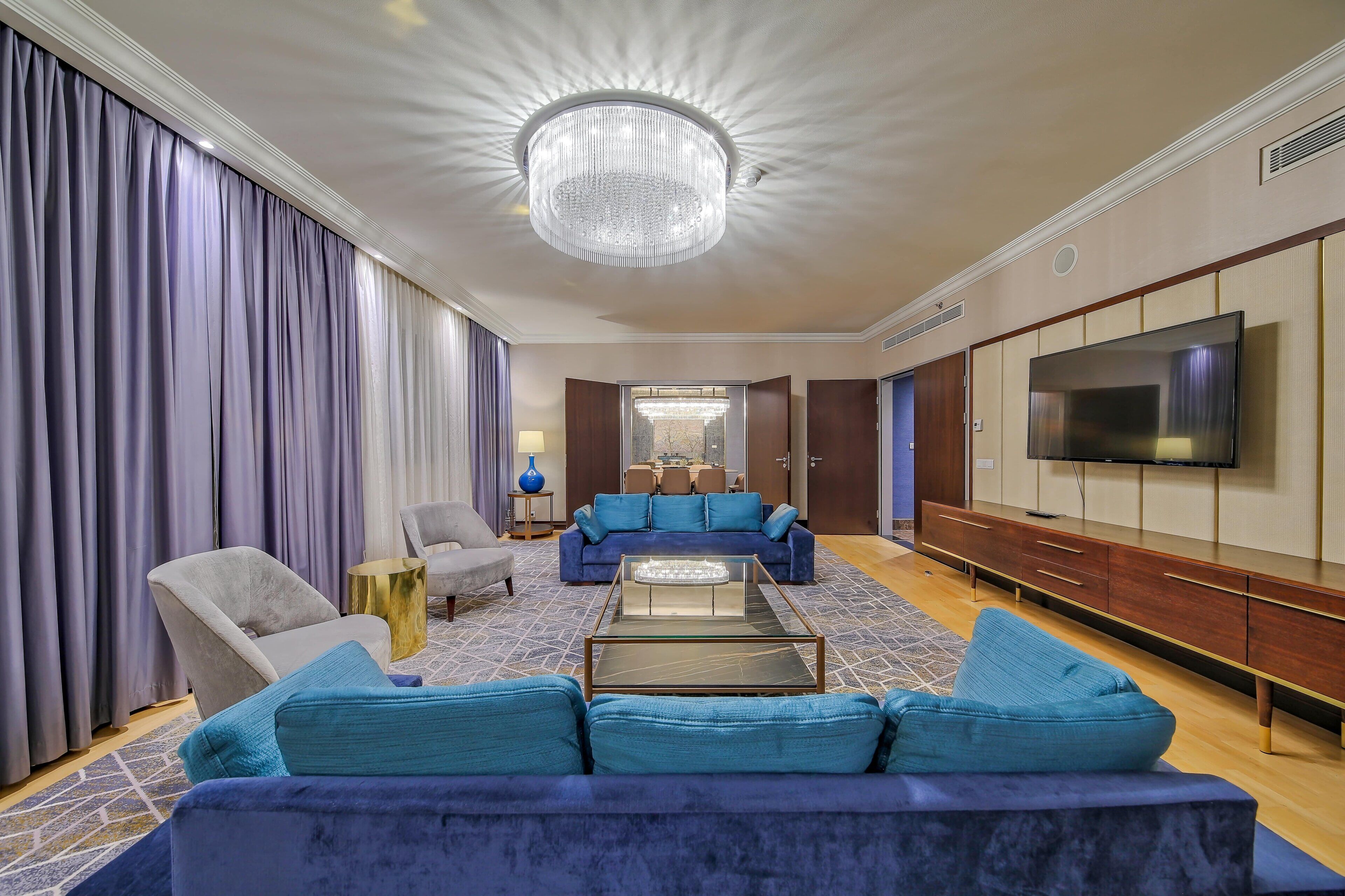 A modern living room with a blue sofa, a glass coffee table, and a flat-screen TV mounted on the wall.