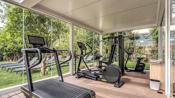 A covered gym area with exercise equipment, large windows, and a view of the outdoors.