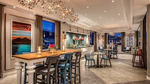 A modern bar area with a wooden countertop, bar stools, and a view of the city at night. - Hotel Mediterraneo (Sant'Agnello)