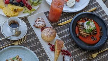 Ein Tisch reichhaltig gedeckt mit verschiedenen Speisen, darunter eine Obstplatte, ein Glas roter Saft, eine Tomate-Mozzarella-Anrichtung, ein Dessert mit Beeren und ein Teller mit roter Soße und Salat.