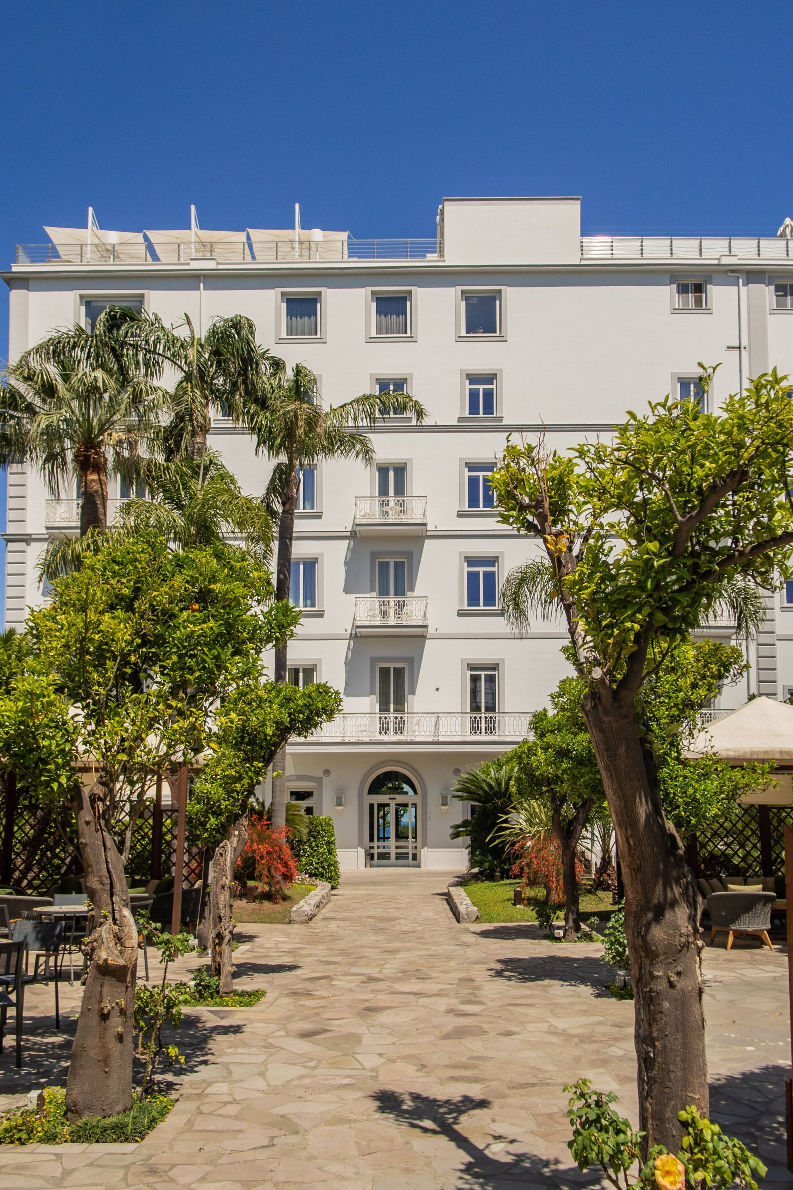 Un edificio a più piani con un ingresso centrale, circondato da un cortile lastricato con alberi e posti a sedere all'aperto.