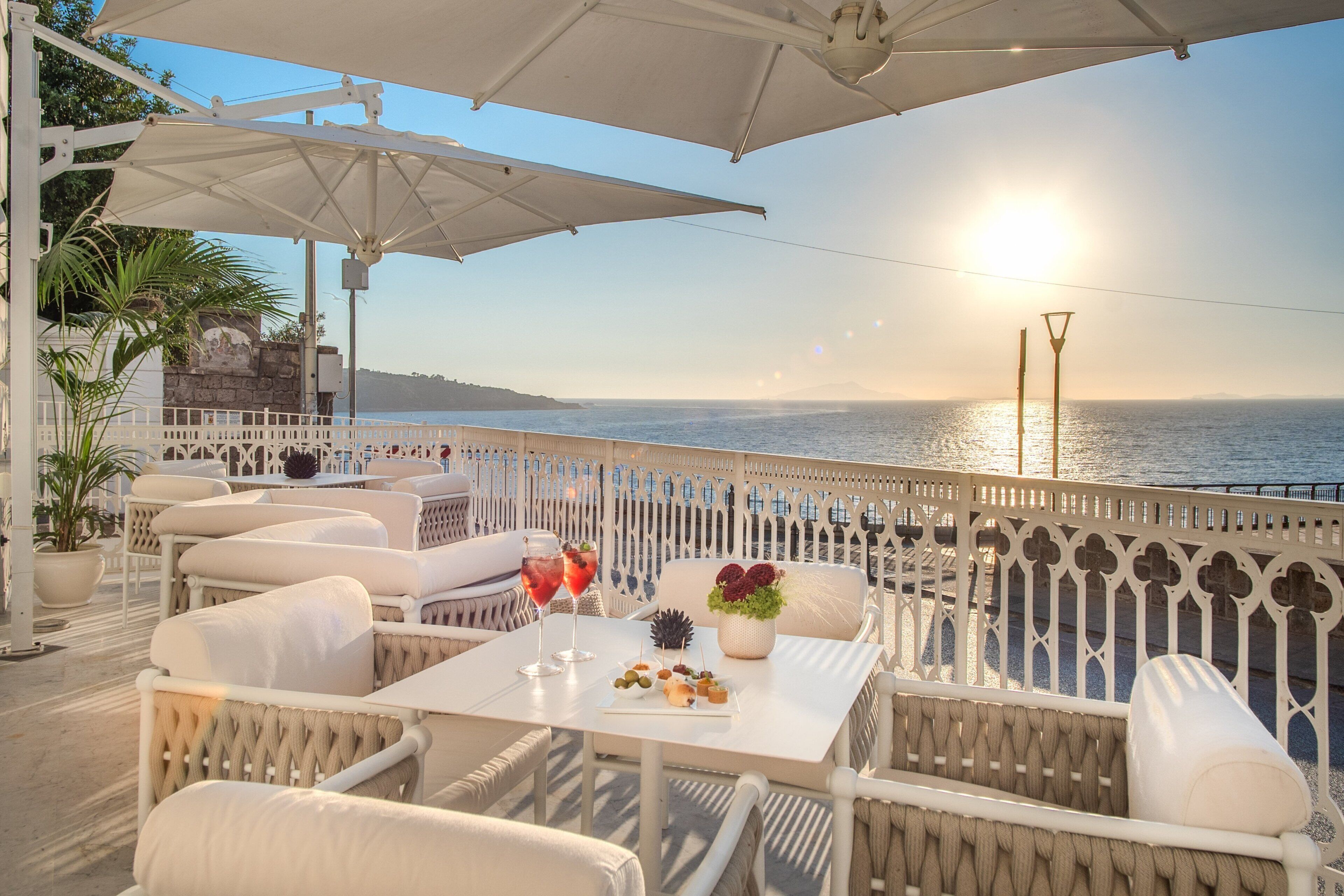 An outdoor seating area with white furniture, a table with snacks and drinks, and a view of the sea.