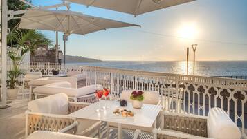An outdoor seating area with white furniture, a table with snacks and drinks, and a view of the sea.
