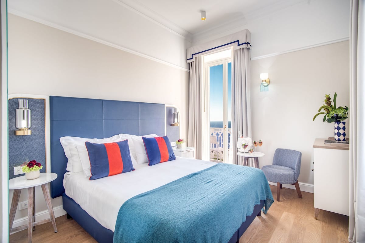Ett hotellrum med en stor säng, ett litet skrivbord, en stol och en balkong med utsikt.