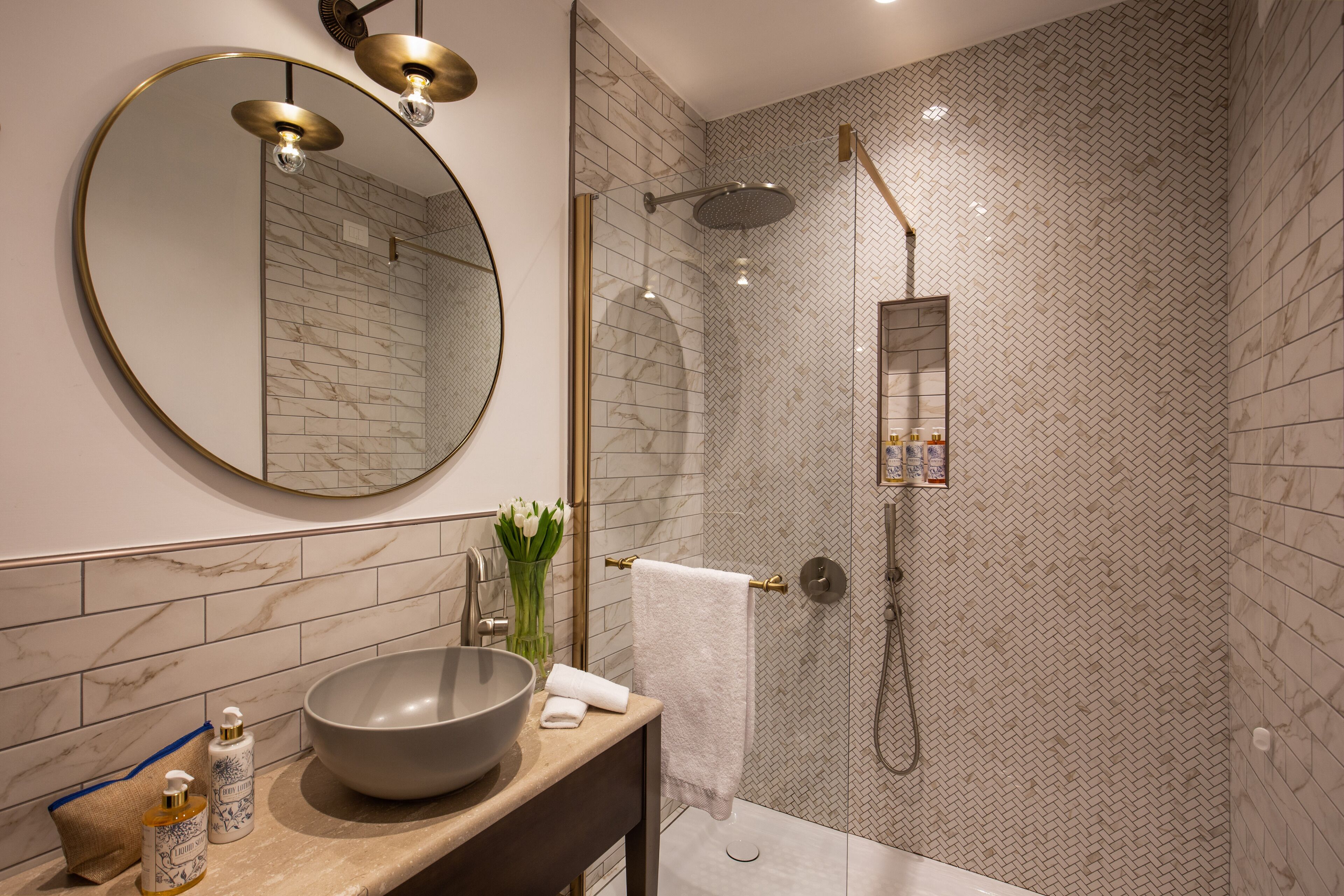 Un bagno moderno con un ampio specchio rotondo, un lavabo a incasso, un soffione a mano e un portasciugamani.