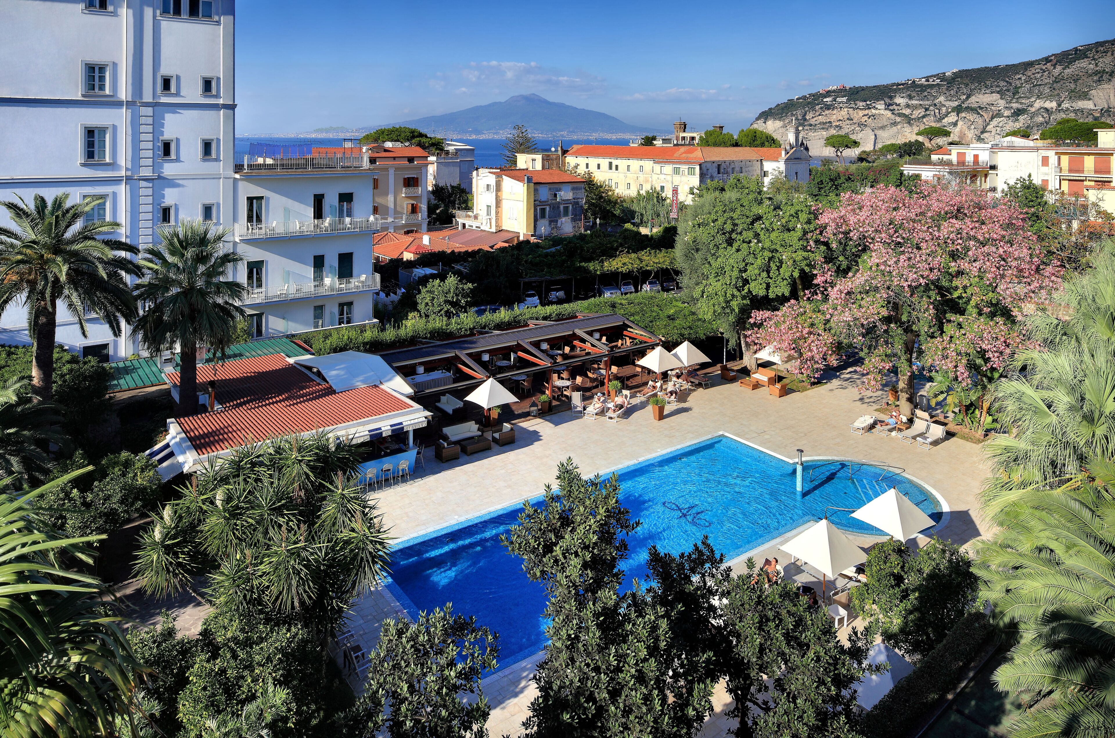 A hotel with a swimming pool, outdoor seating, and a view of a mountain.