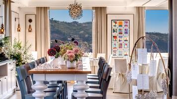 A dining area with a long table, chairs, and a view of the hills.