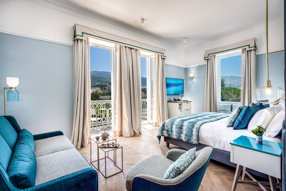Ett modernt hotellrum med en stor säng, ett skrivbord, en soffa och en balkong med utsikt över kullarna.