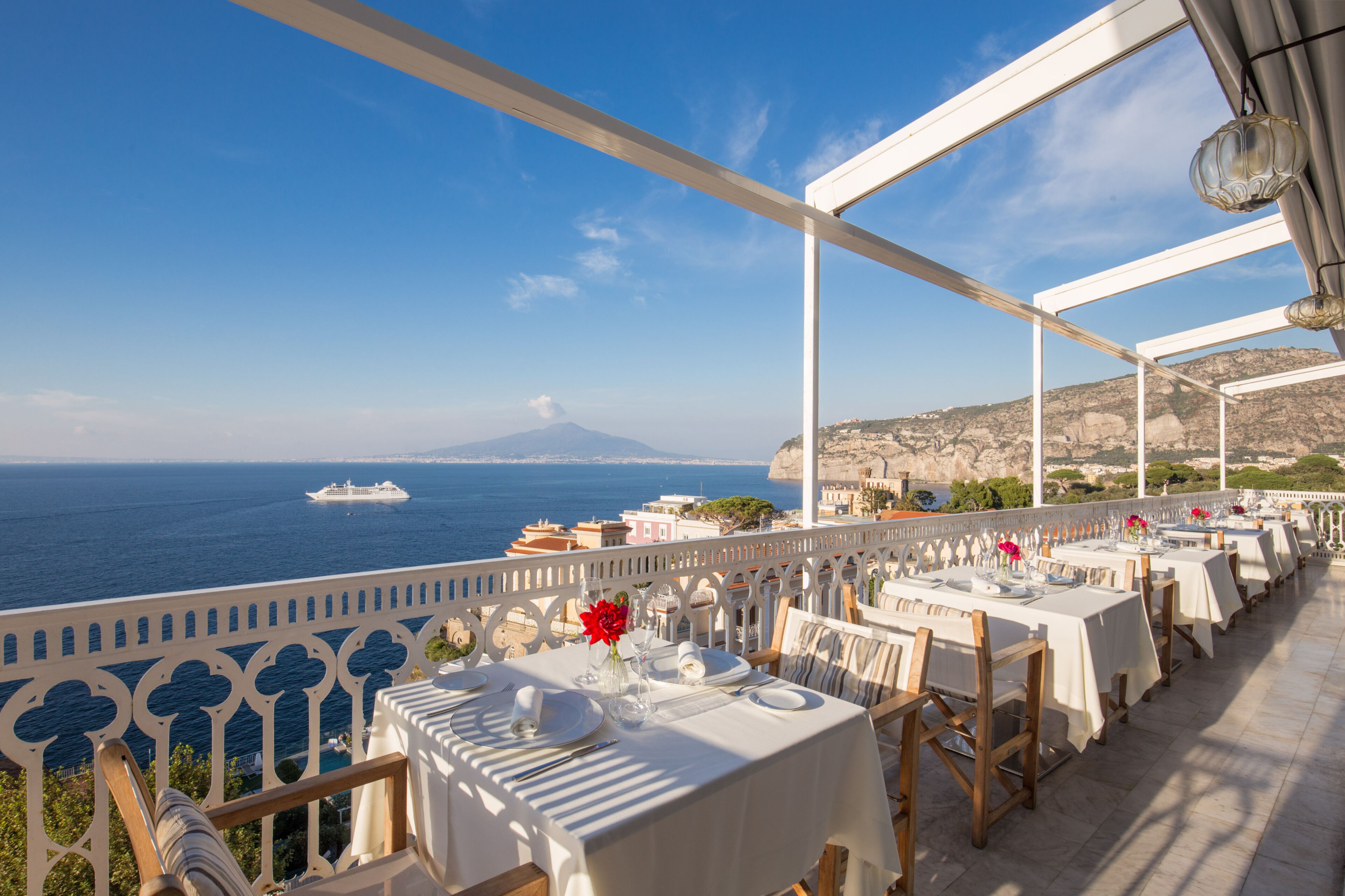 A seaside restaurant with tables set for dining, overlooking the ocean and a distant mountain.