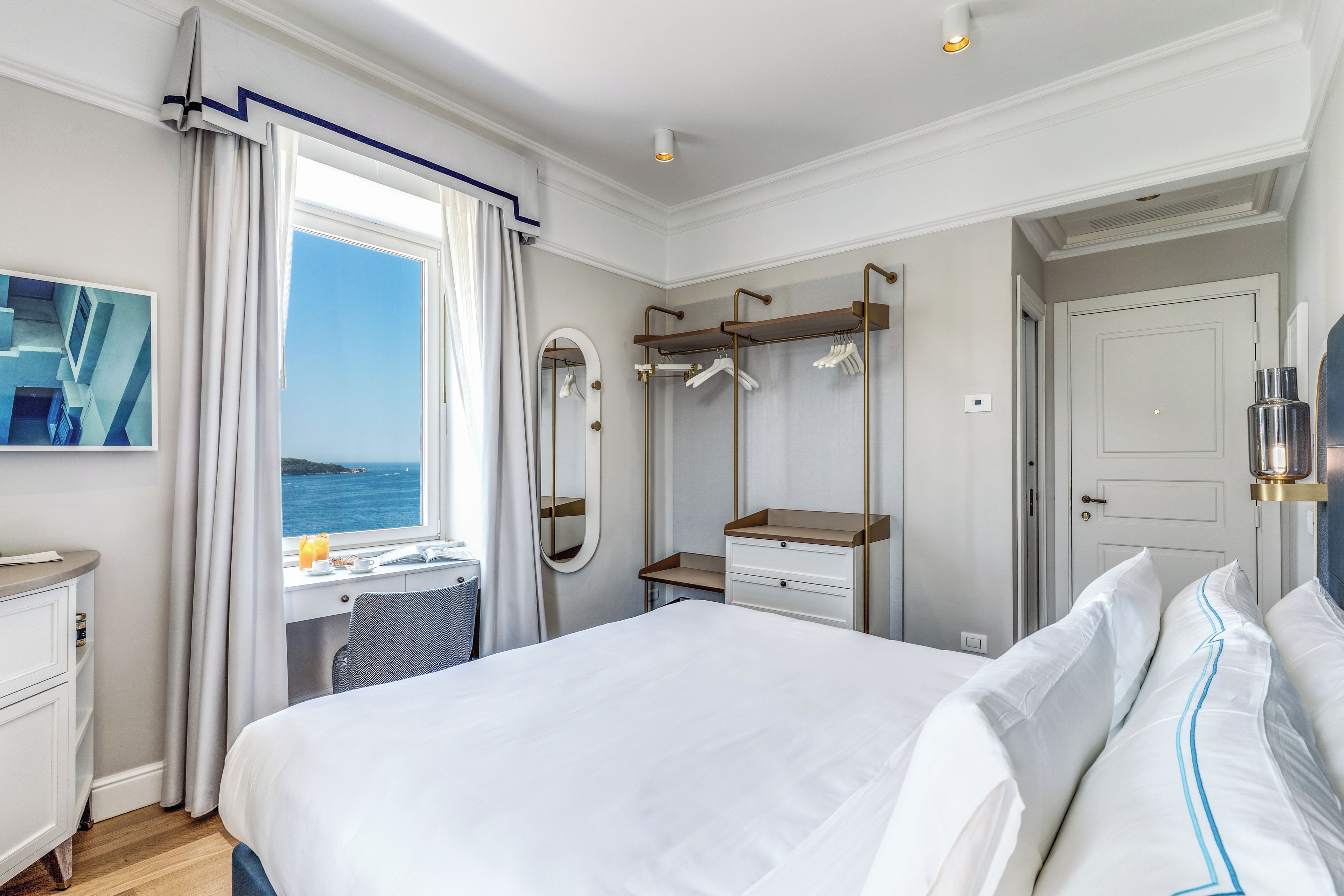 Une chambre d’hôtel avec un lit, un bureau, un miroir et une vue sur la mer.