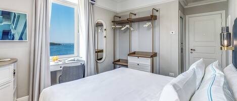 Une chambre d’hôtel avec un lit, un bureau, un miroir et une vue sur la mer.