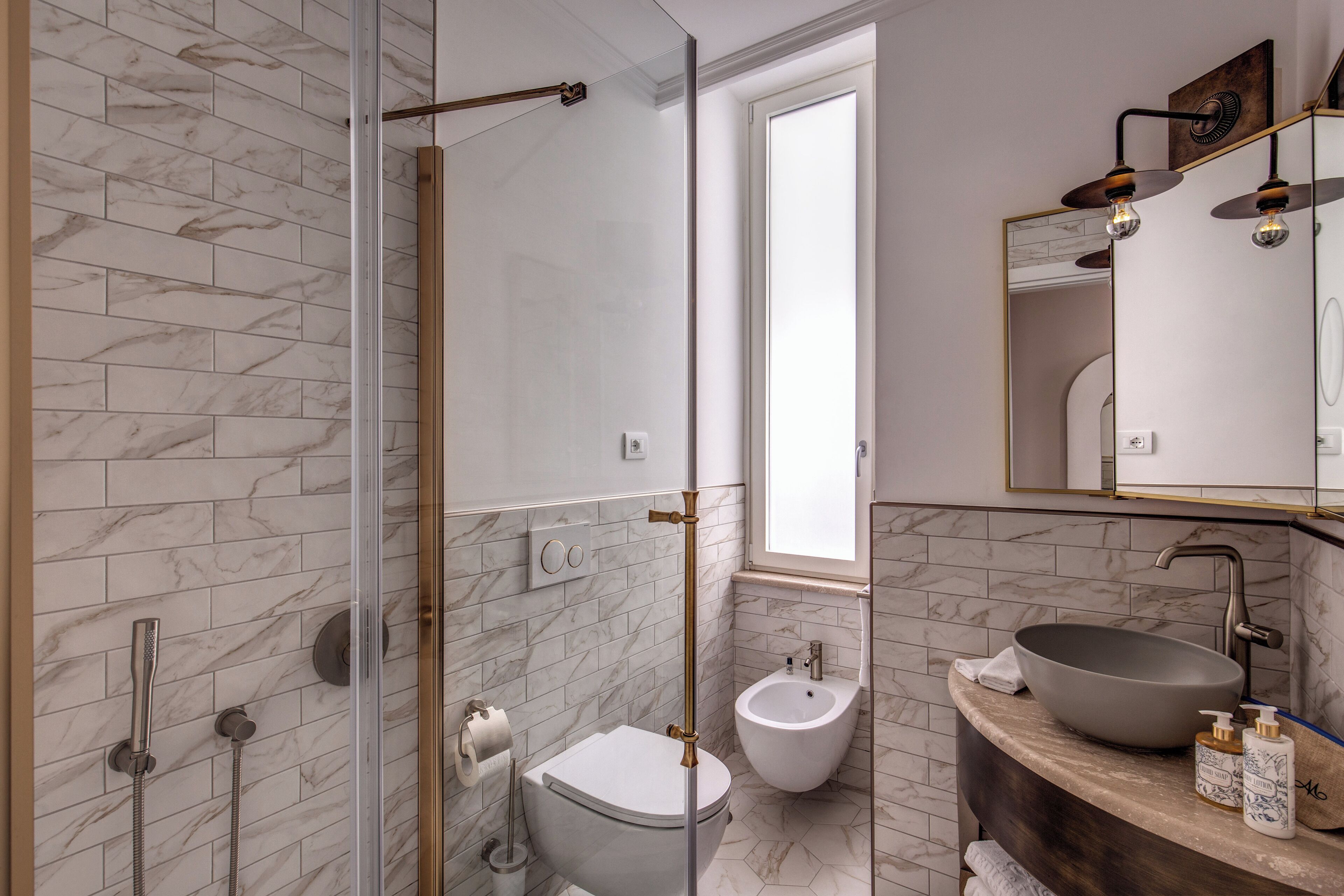 A bathroom with a glass shower enclosure, a toilet, a bidet, and a vanity with a large sink and mirror.