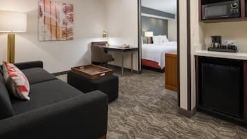 A hotel room with a sofa, a desk, a bed, a microwave, and a coffee maker.