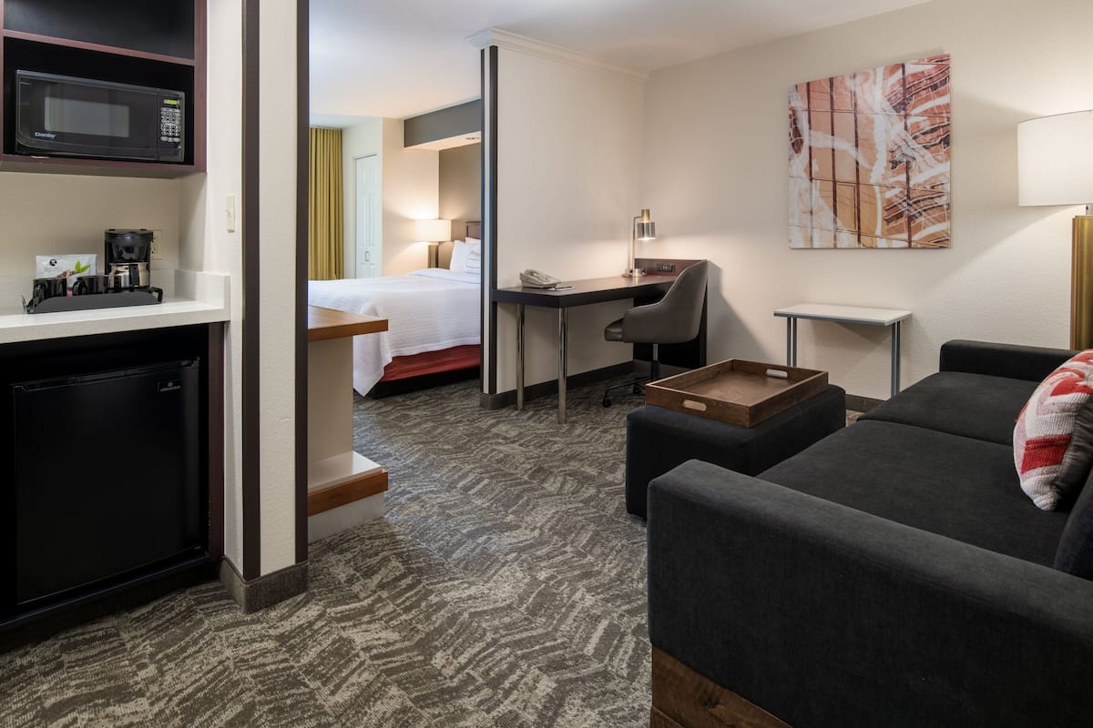 A hotel room with a kitchenette, a bed, a desk, and a sofa.