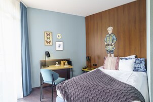 Habitación de hotel con cama, escritorio, silla y pared con paneles de madera y obra de arte de mariposas.