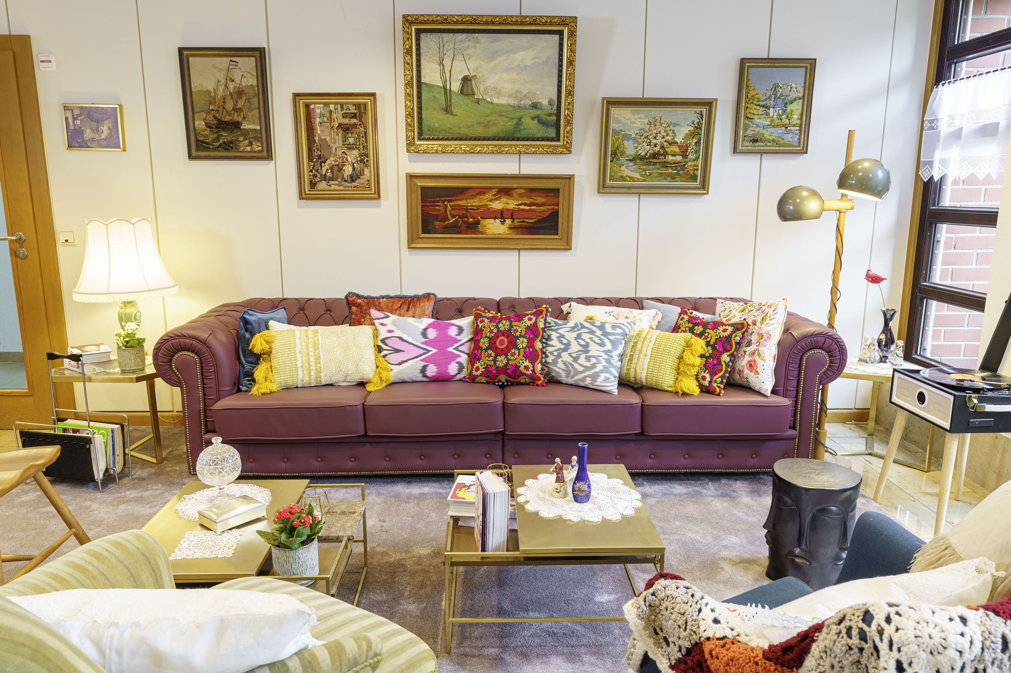 A living room with a purple sofa, various cushions, a coffee table, and a bookshelf.