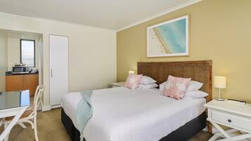 Un dormitorio con una cama grande, una mesita de noche con lámpara, una silla, un escritorio y un microondas en la esquina.