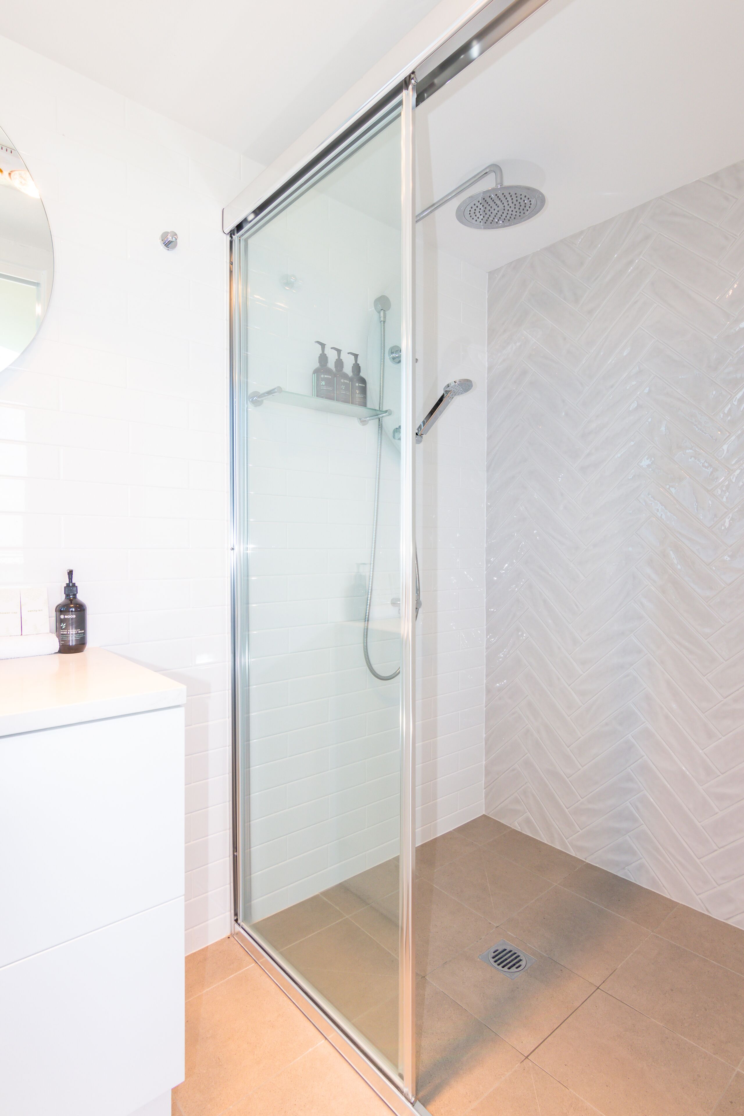 Un baño moderno con ducha de vidrio, lavamanos blanco y pared con patrón de espiga.