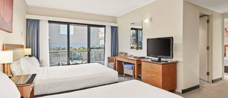 A hotel room with two beds, a desk with a TV, a chair, and a balcony with curtains.