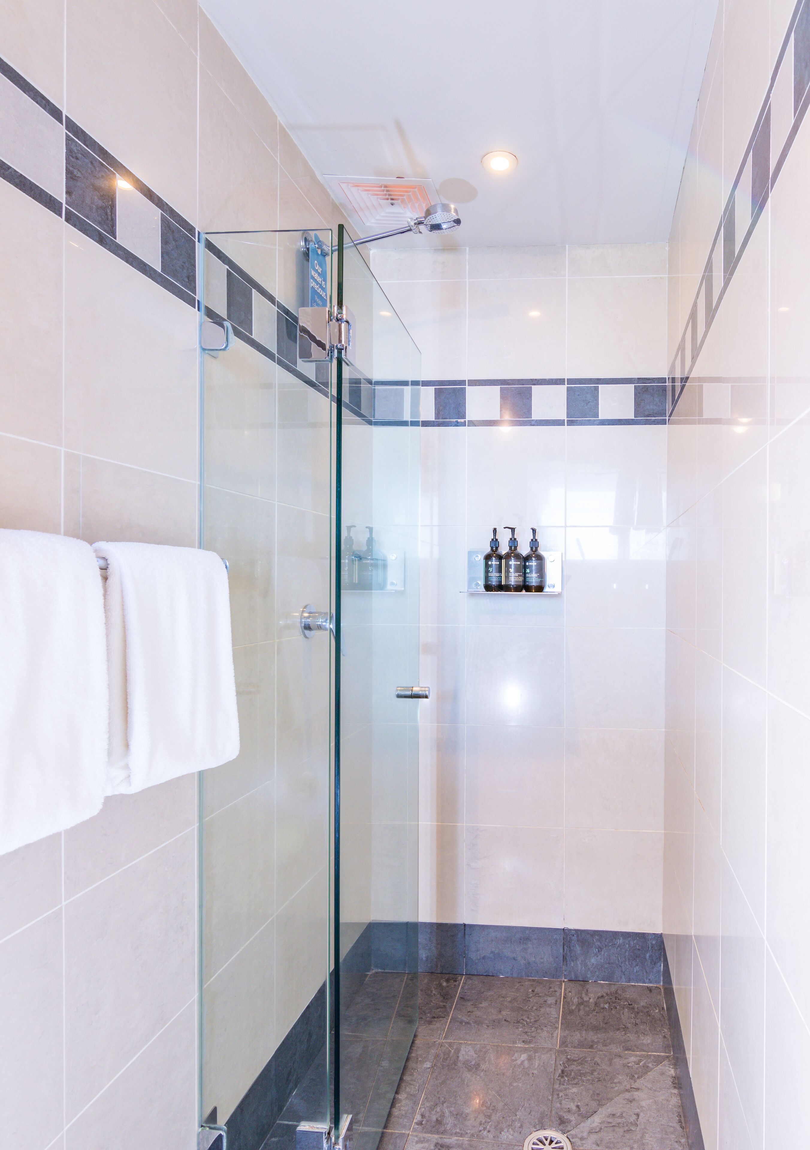 Une salle de bain moderne avec une douche à parois de verre, des carreaux blancs et gris, et une étagère contenant des articles de toilette.