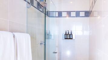 Une salle de bain moderne avec une douche à parois de verre, des carreaux blancs et gris, et une étagère contenant des articles de toilette.