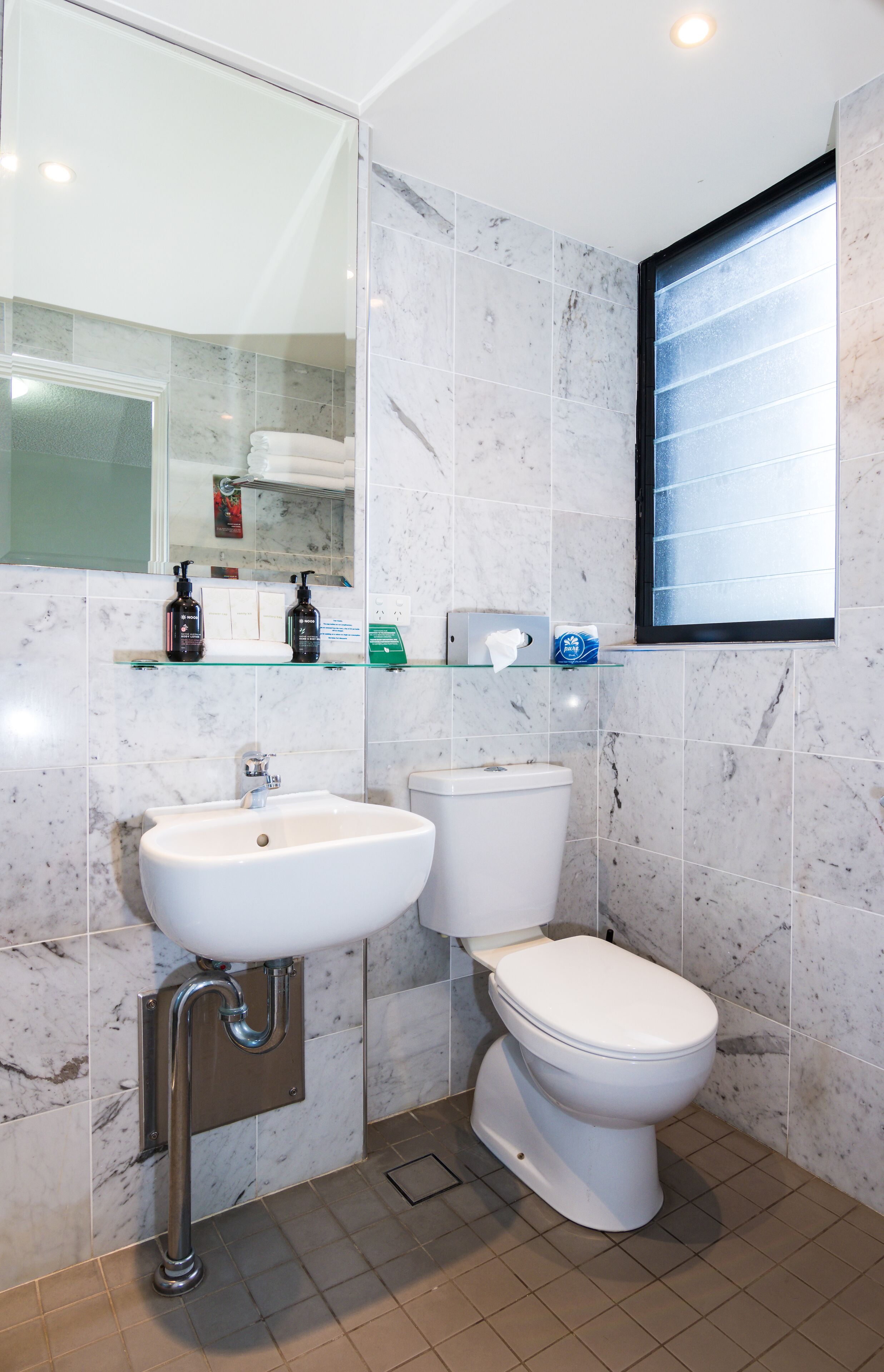 A bathroom with a white sink, toilet, and a glass shelf with toiletries.