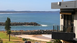 Una proprietà sul lungomare con un balcone vista oceano, un molo di roccia e una spiaggia di sabbia.