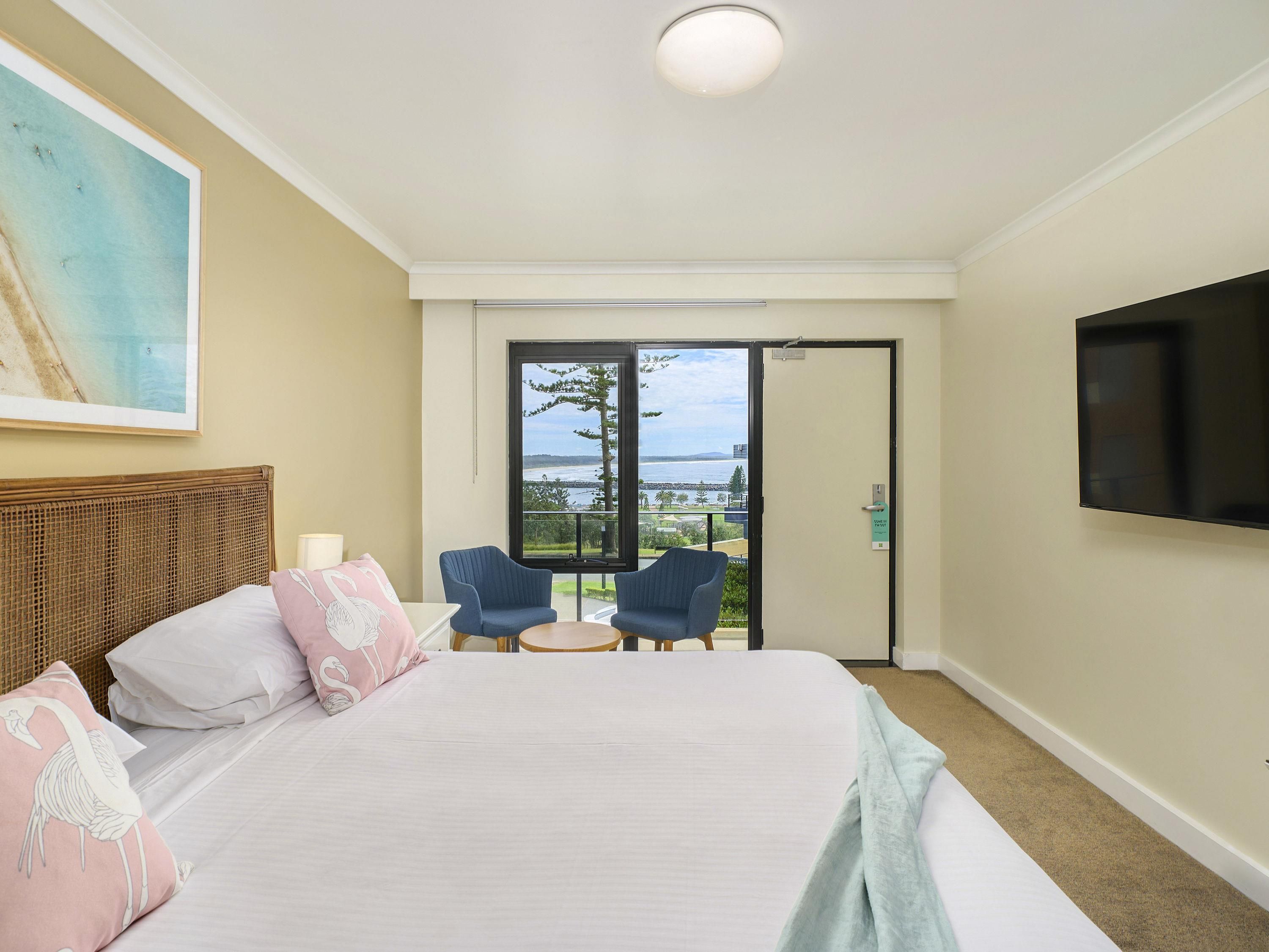 Habitación de hotel con una cama grande, dos sillones, un televisor y un balcón con vistas.