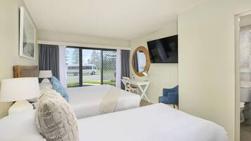 Habitación de hotel con dos camas, un escritorio con silla, televisión y vista a la calle.